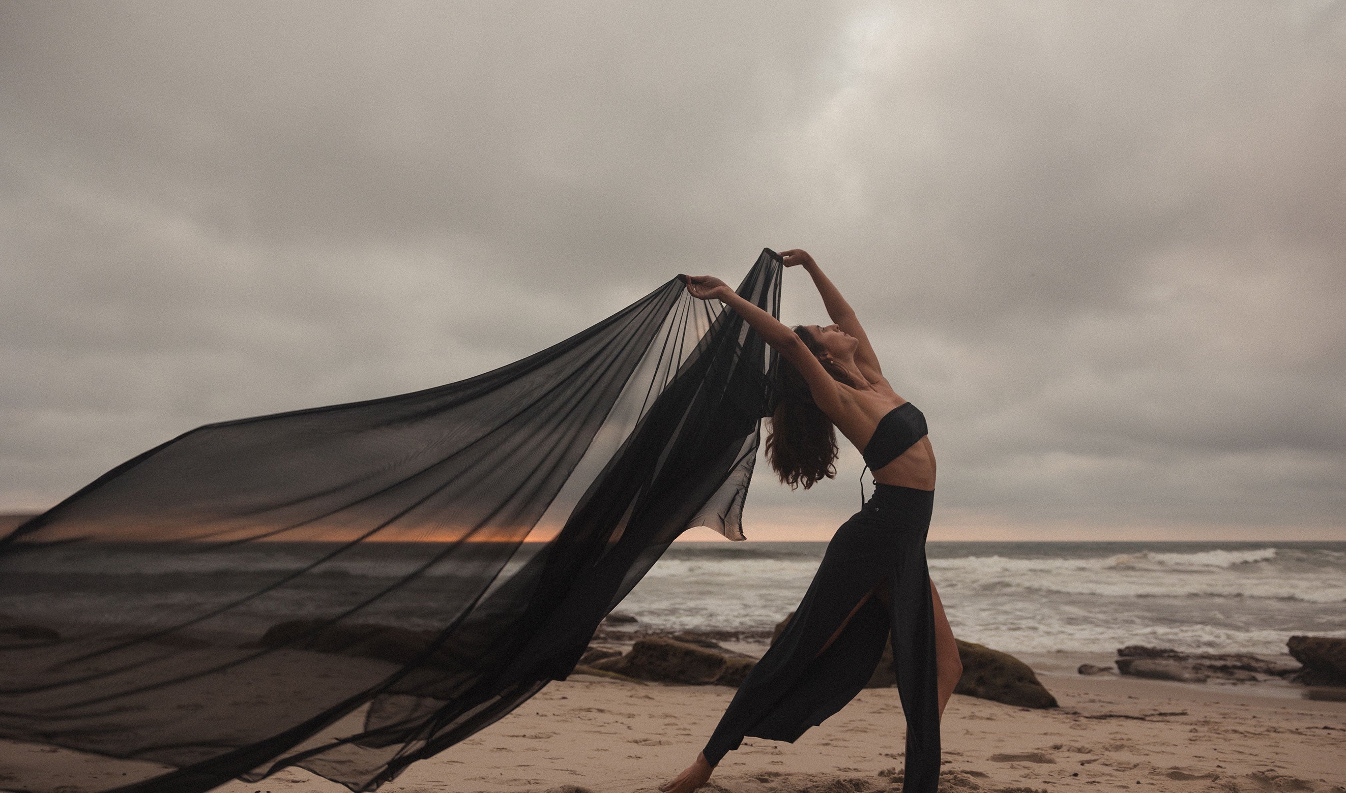 Model on the beach wearing a black Windwrap Skirt and Belle Bandeau Top.
