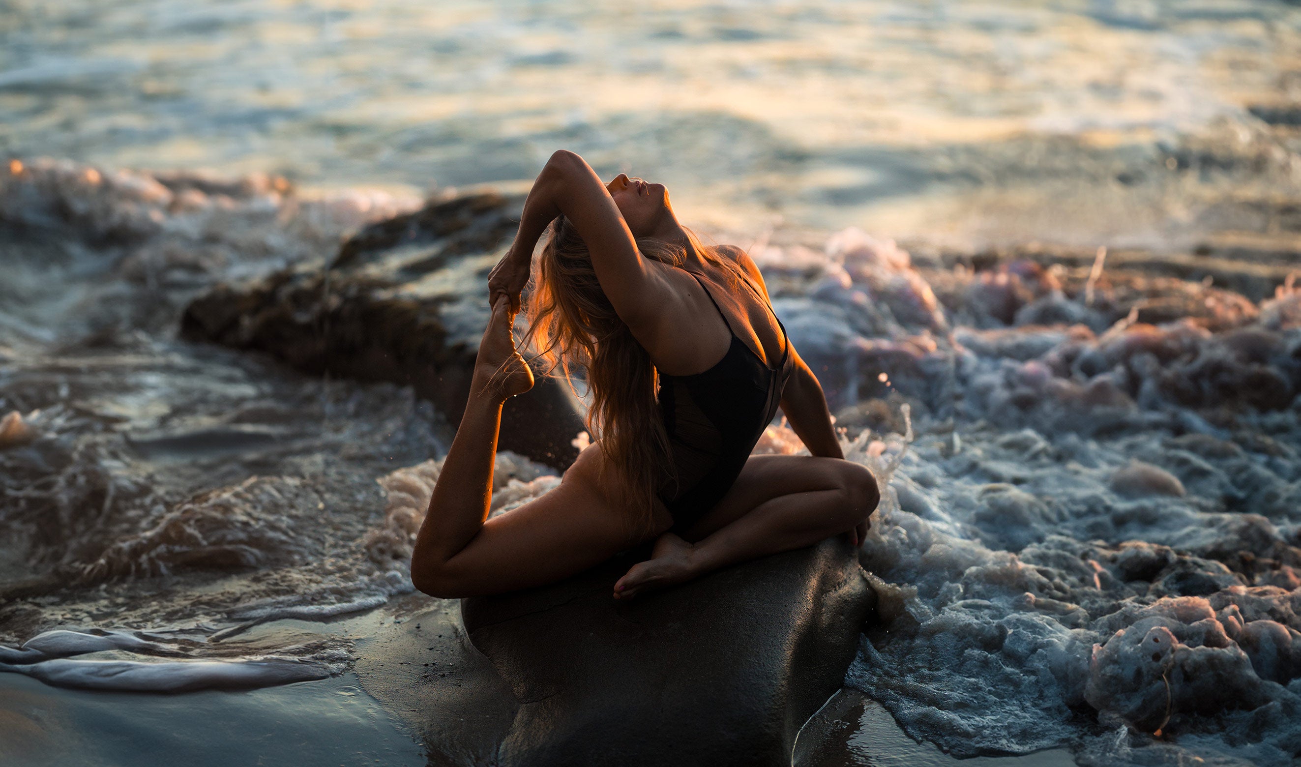 Model sitting on a rock by the ocean at sunset