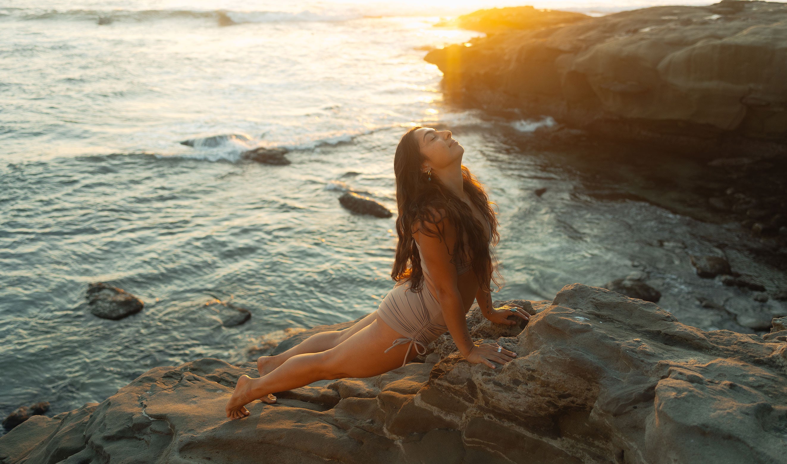Model sitting on a rocky beach at sunset