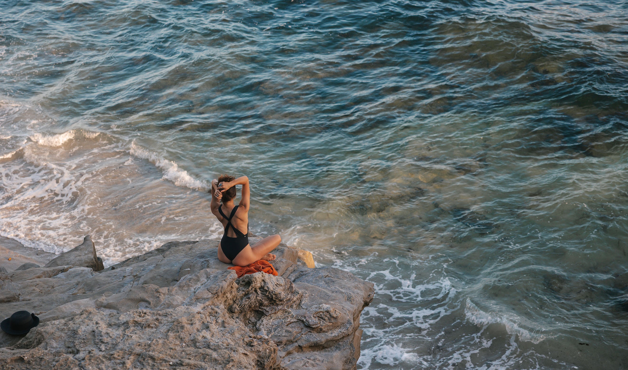 Model sitting on a rock by the ocean with waves crashing around