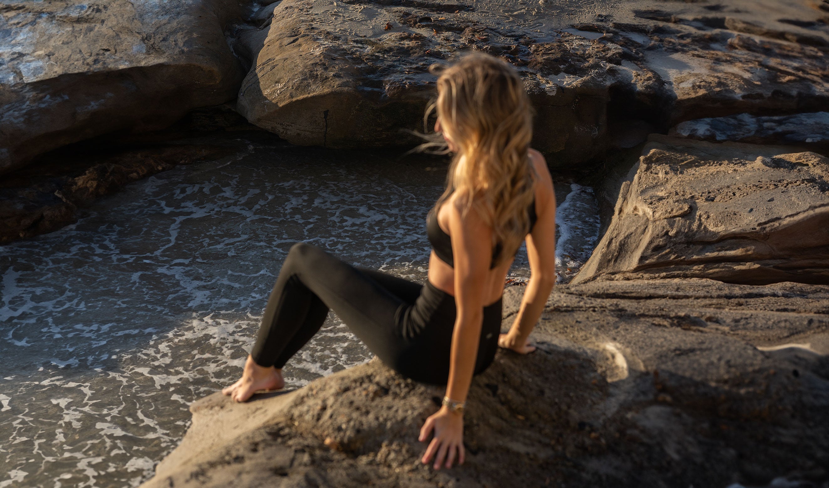 Woman wearing Mika Leggings sitting on a rock by the water at sunset